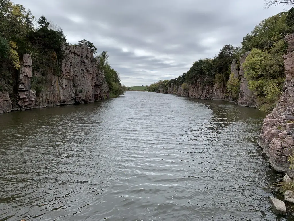 View down a creek with rocky and vegetation-covered walls on both sides; grey, cloudy sky.