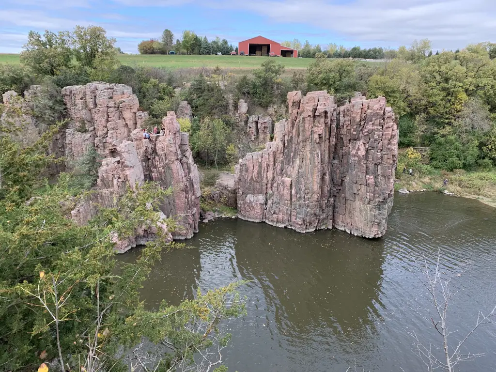 View is from above. Creek is below with rock walls on the far side. Above the rocks sits a red barn on a nearby hill.