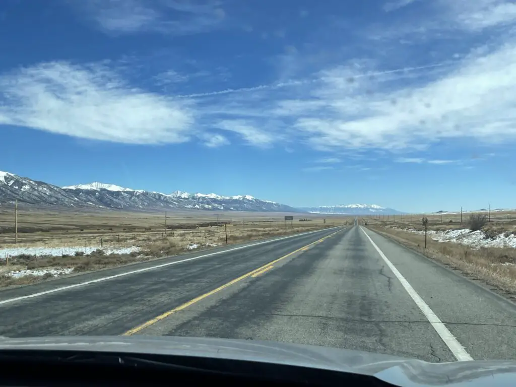 Looking down the road at the long San Luis Valley. Snow-covered Sangre de Cristo mountains on the left.