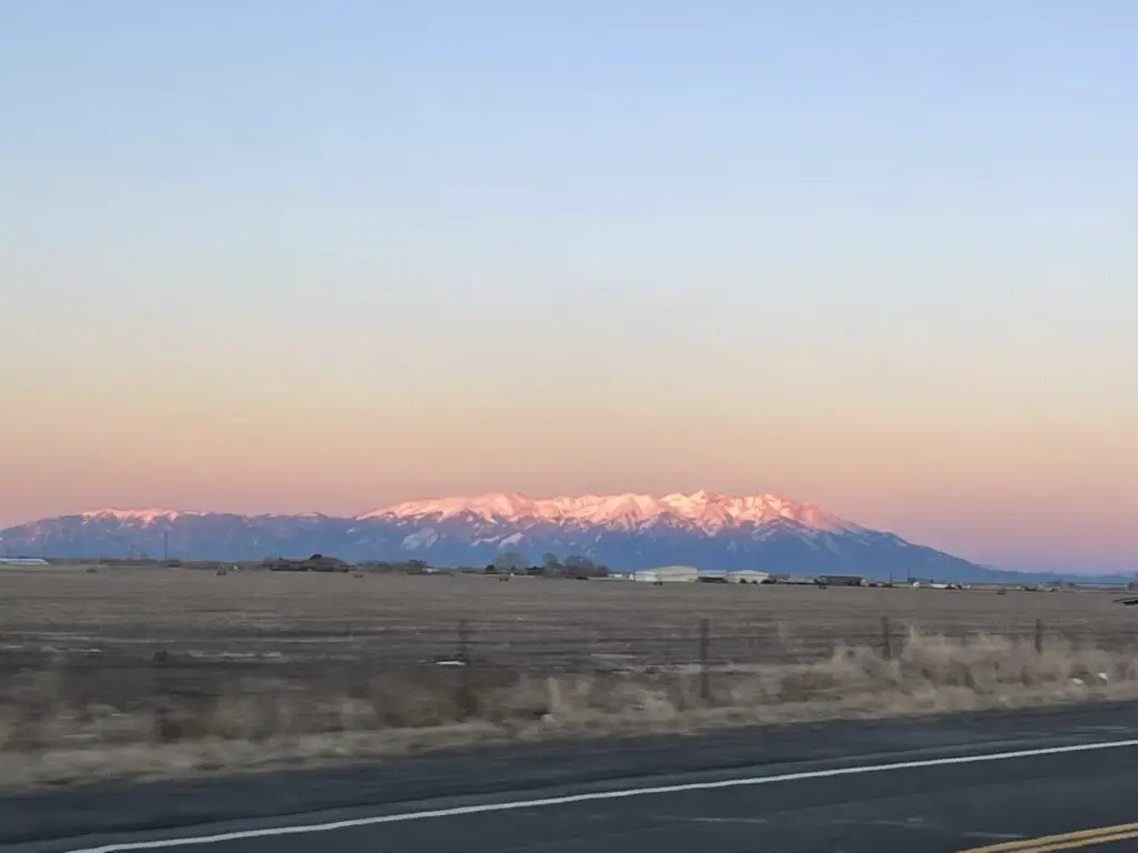 Pastureland backed by snow-covered mountains that are pink as they reflect the setting sun