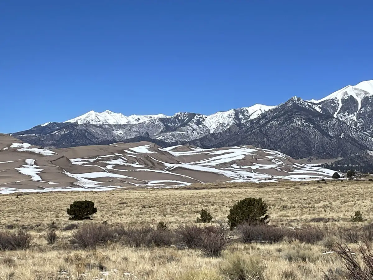 Snow-covered pasture and sand dunes with snow-topped Sangre de Cristo mountains in background