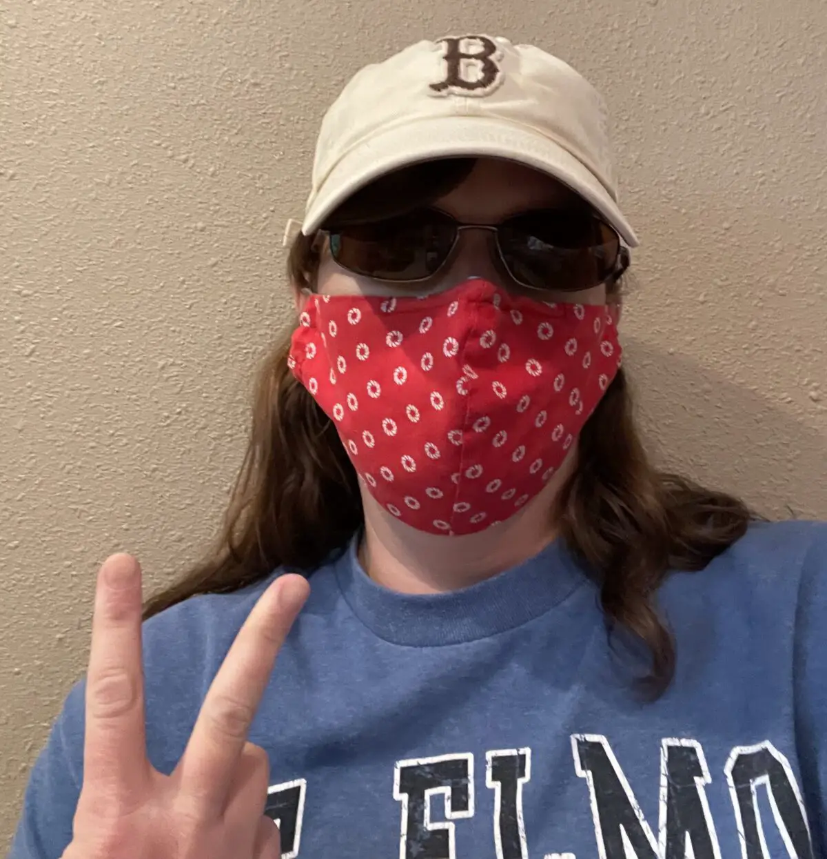 Woman with mask covering face makes a hand gesture with the number 2