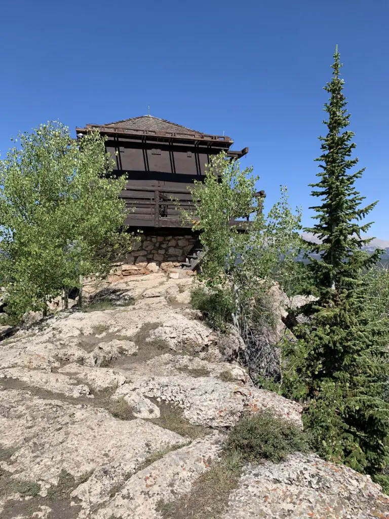 A wooden and shuttered fire tower sits on top of rocks. Trees grow out of the rocks.
