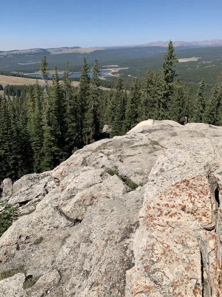 Mountain overlook, rock and trees in the foreground, then a lake and mountains in the background