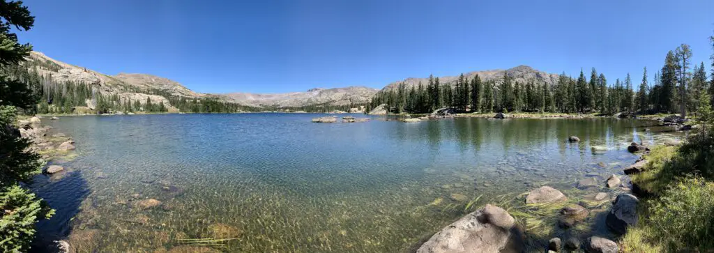 Panoramic view of a blue, peaceful lake with rocky mountains and trees in the background