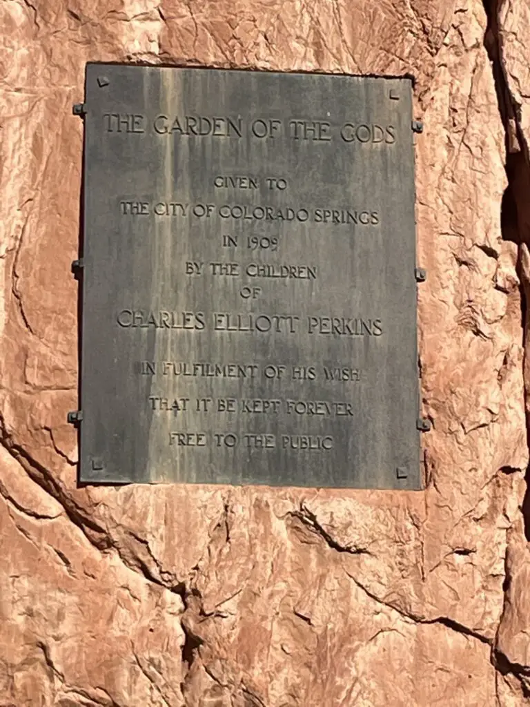 Black sign against red rock that reads, "The Garden of the Gods given to the city of Colorado Springs in 1909 by the children of Charles Eliott Perkins in fulfilment of his wish that it be kept forever free to the public." 