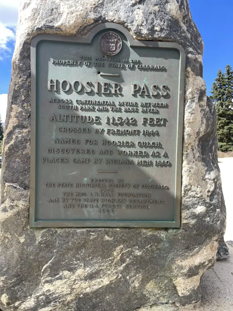 Metal sign set into a tall, narrow rock reads, "Hoosier Pass across Continental Divide between South Park and the Blue River. Altitude 11,542 feet. Named for Hoosier Gulch discovered and worked as a placer (gold) camp by Indiana men 1880".