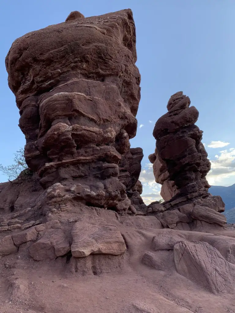 Two tall, narrow, red rock formation rise off a flatter rock formation