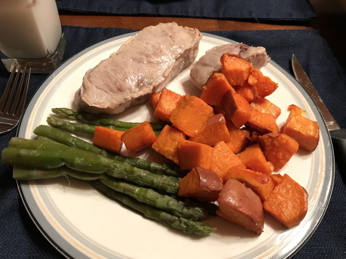 Cooked sweet potatoes, pork and asparagus on a plate