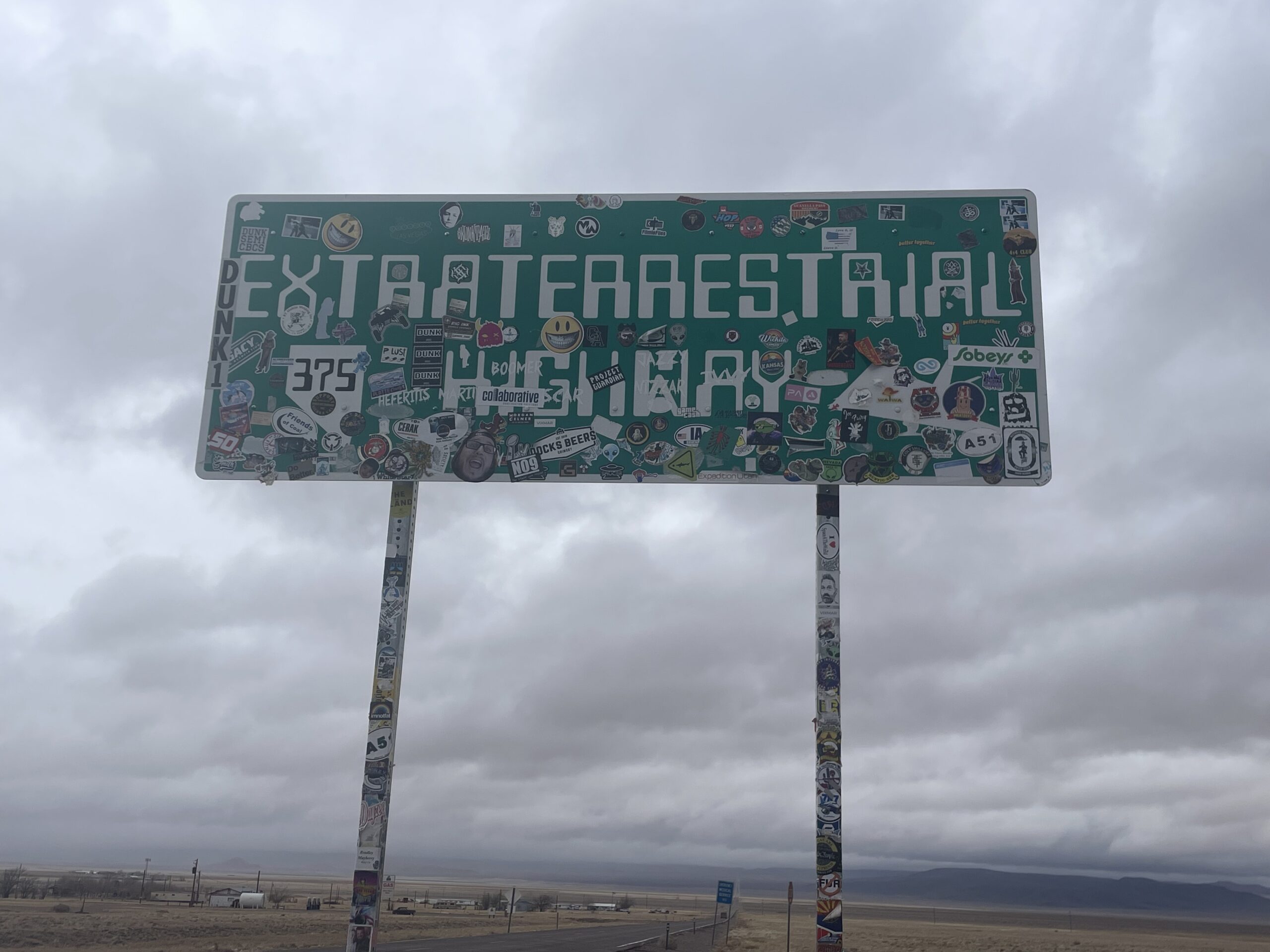 Green road sign covered in stickers. The words "Extraterrestrial Highway" are barely visible through the stickers. 