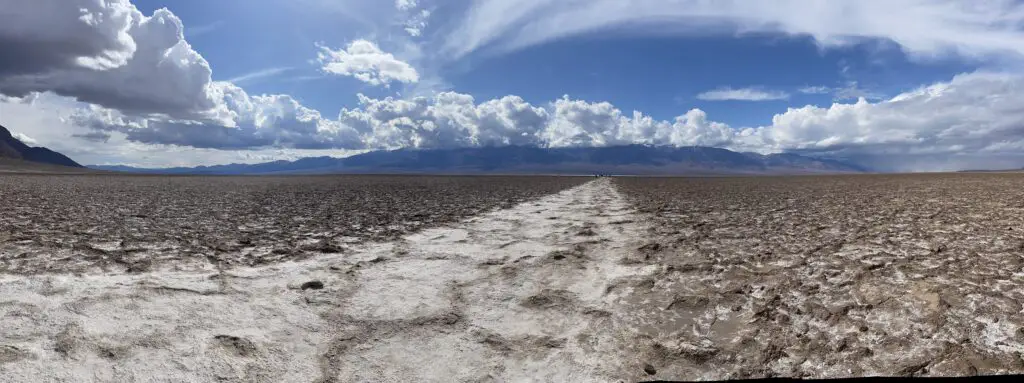 Panoramic picture of a flat valley, filled with a salt-flat, and sand and surrounded by rocky mountains.