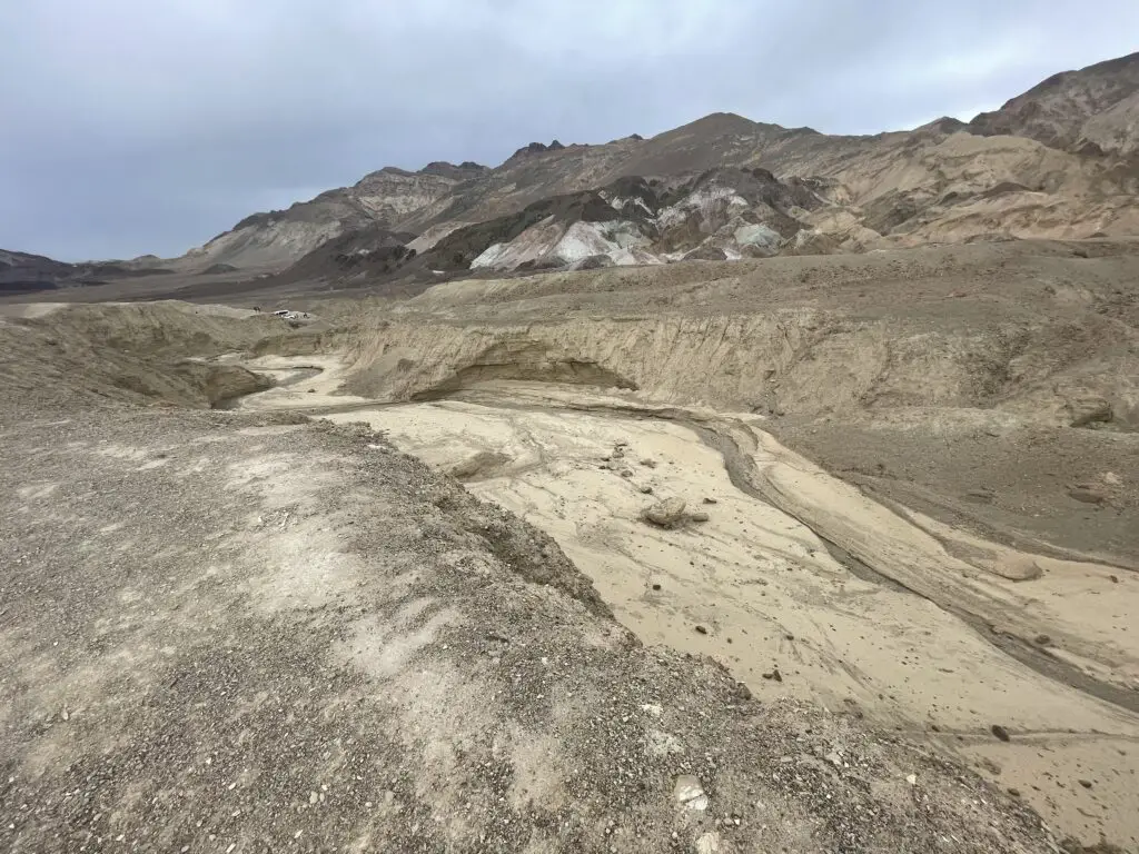 Brown and tan gravel in a dry wash area, hills in the background are made from dark brown, tan, white and red-brown dirt.