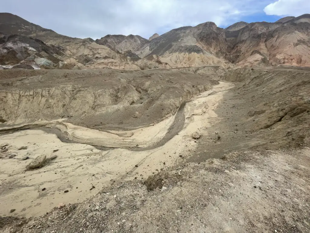 Brown and tan gravel in a dry wash area, hills in the background are made from dark brown, tan, and red-brown dirt.