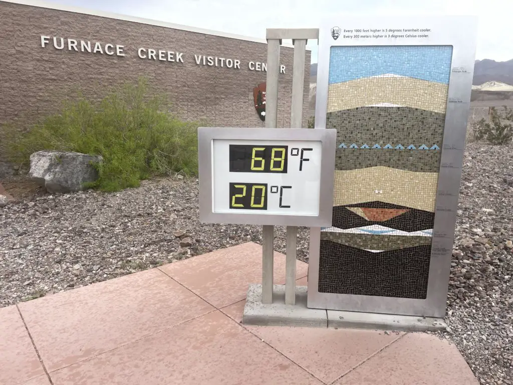 A digital thermometer on a sign reads 68 Fahrenheit, 20 Celsius. The sign on the building reads, Furnace Creek Visitor Center