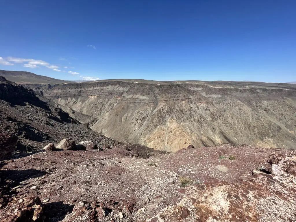 Rocky, short, narrow canyon with red, brown, and tan gravel, all under a clear, blue sky. 