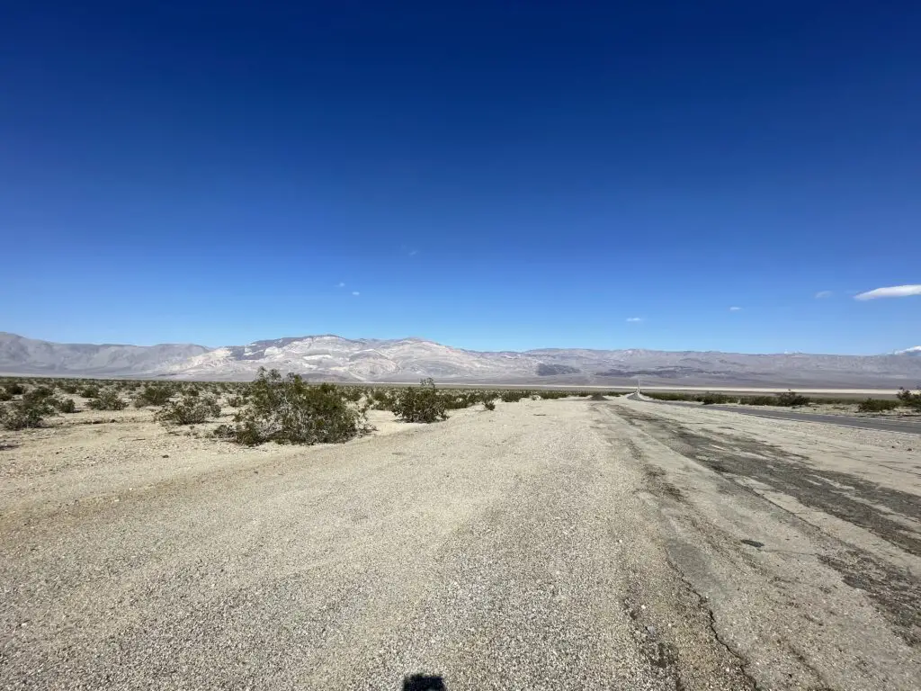 Rocky, flat desert (with scrub brush) surrounded by rocky mountains in the distance, all under a clear, cerulean sky