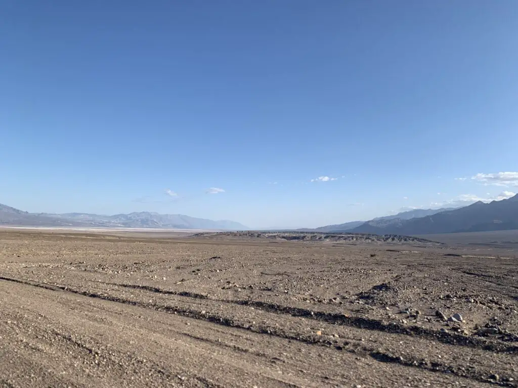 Flat, brown, rocky valley surrounded by rocky mountains, all under a clear, blue sky