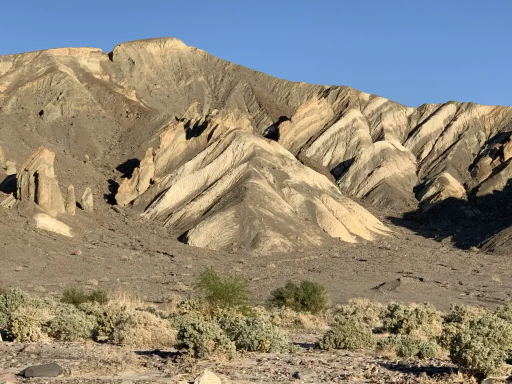 Yellow-colored hills lead to a mountain in the background, greenish scrub brush is in the foreground. 