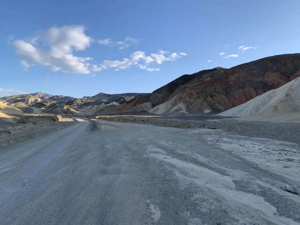 Grey-gravel road, in-shadow, with brown hills rising in the background