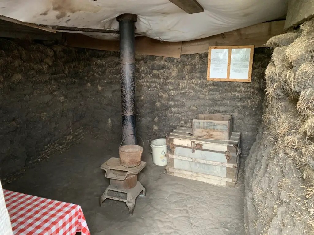 A small table, iron stove and wooden dressing inside a rock and mud duggout house