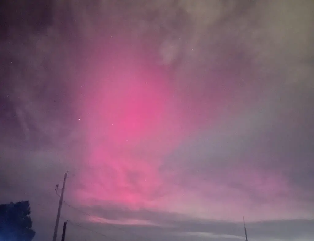 Rosy pink and blue-green light spreads across a dark, night sky. 