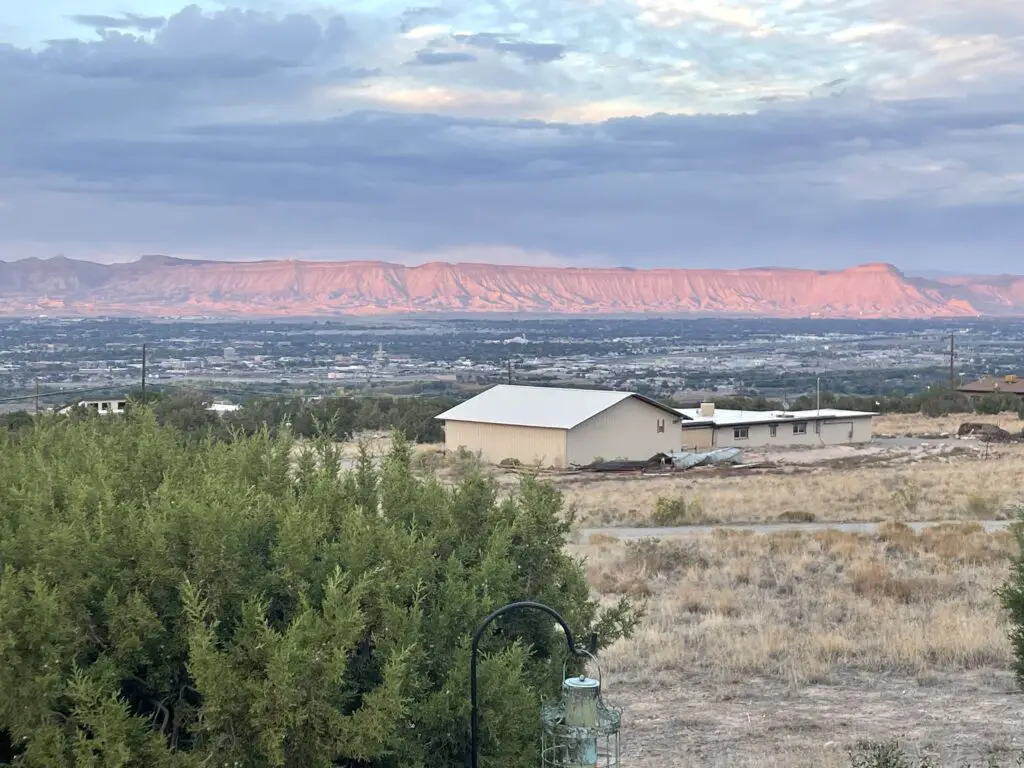 Dry, rocky cliffs that resemble books sitting on a shelf and lit pink by the sunset sit in the far background with a metro area spread in the foreground. 