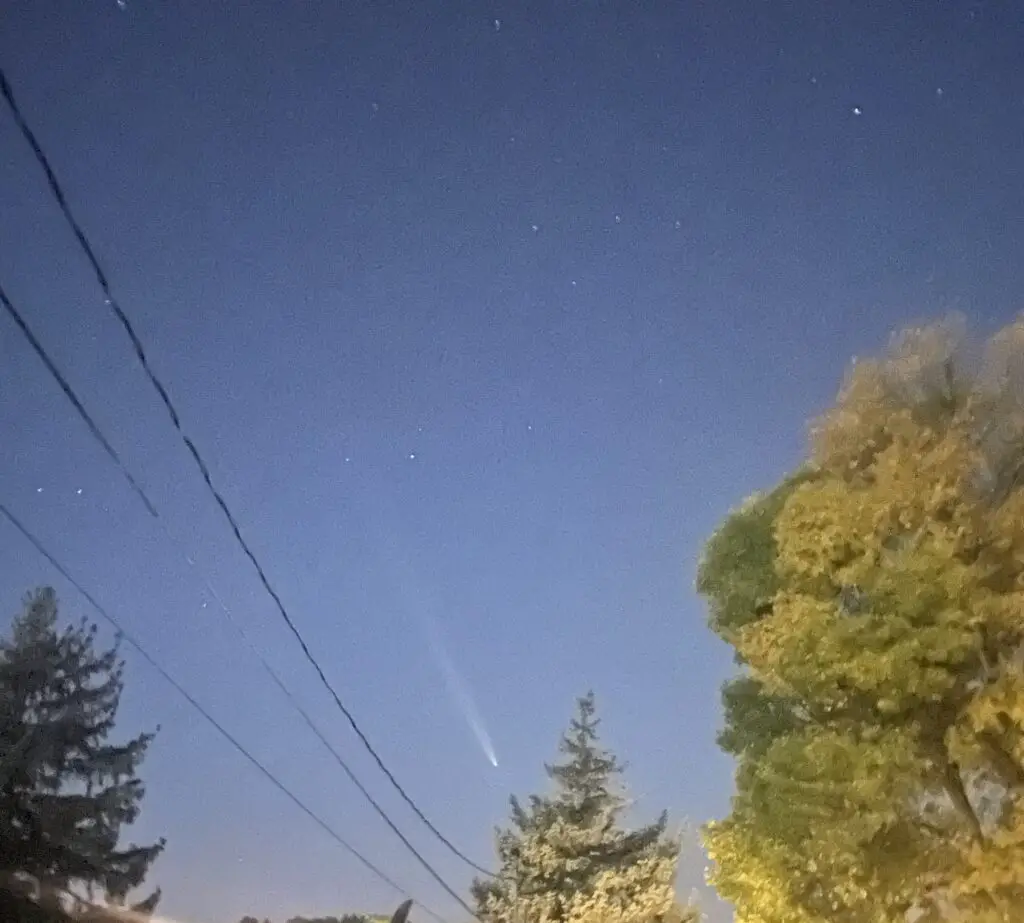 Light comet tail flies across a dark, night sky