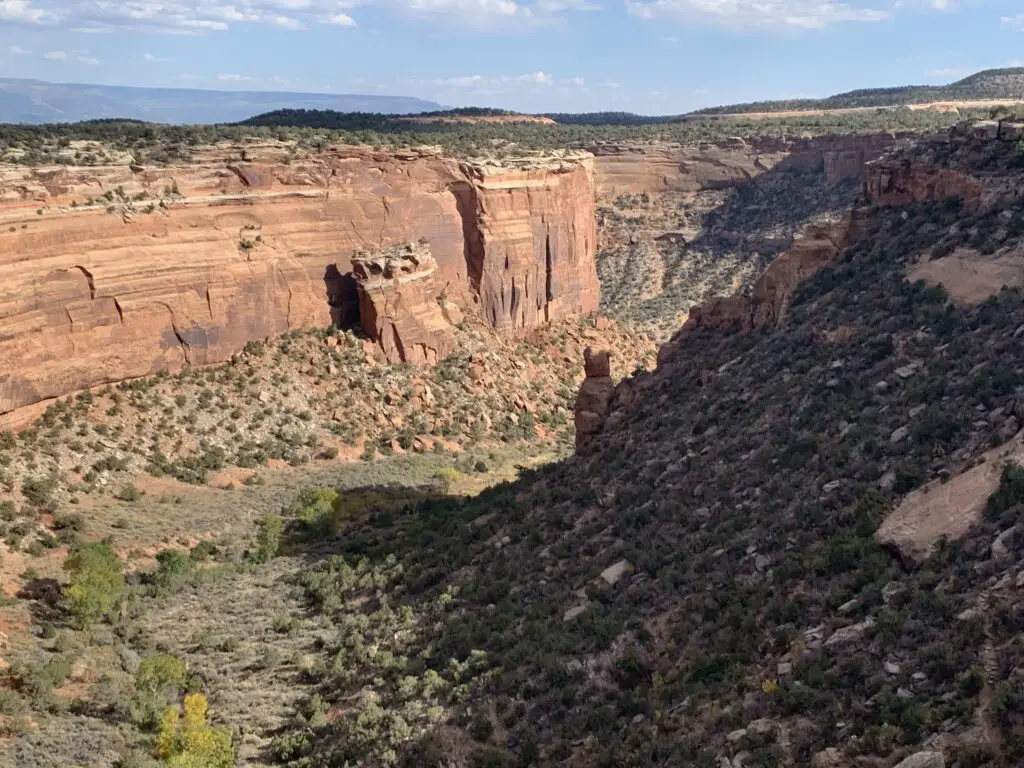 Large, rock boulder fallen off a rocky cliff and sitting on the floor of a scrub-brush covered canyon floor