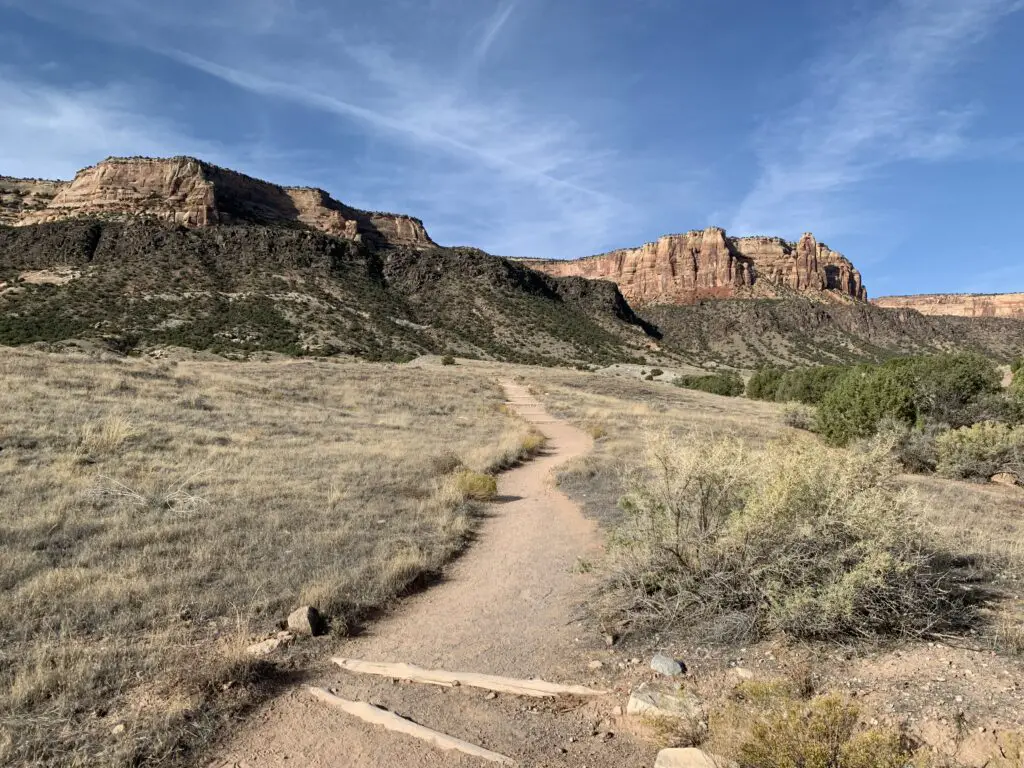 Rocky, gray cliffs tower over green, scrub brush covered rock and grassland