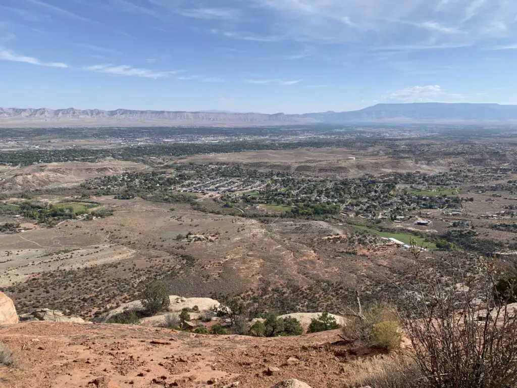 Tall, rocky cliffs in the background with trees and a small city amongst a drier, desert-like environment in the foreground, as seen from above.