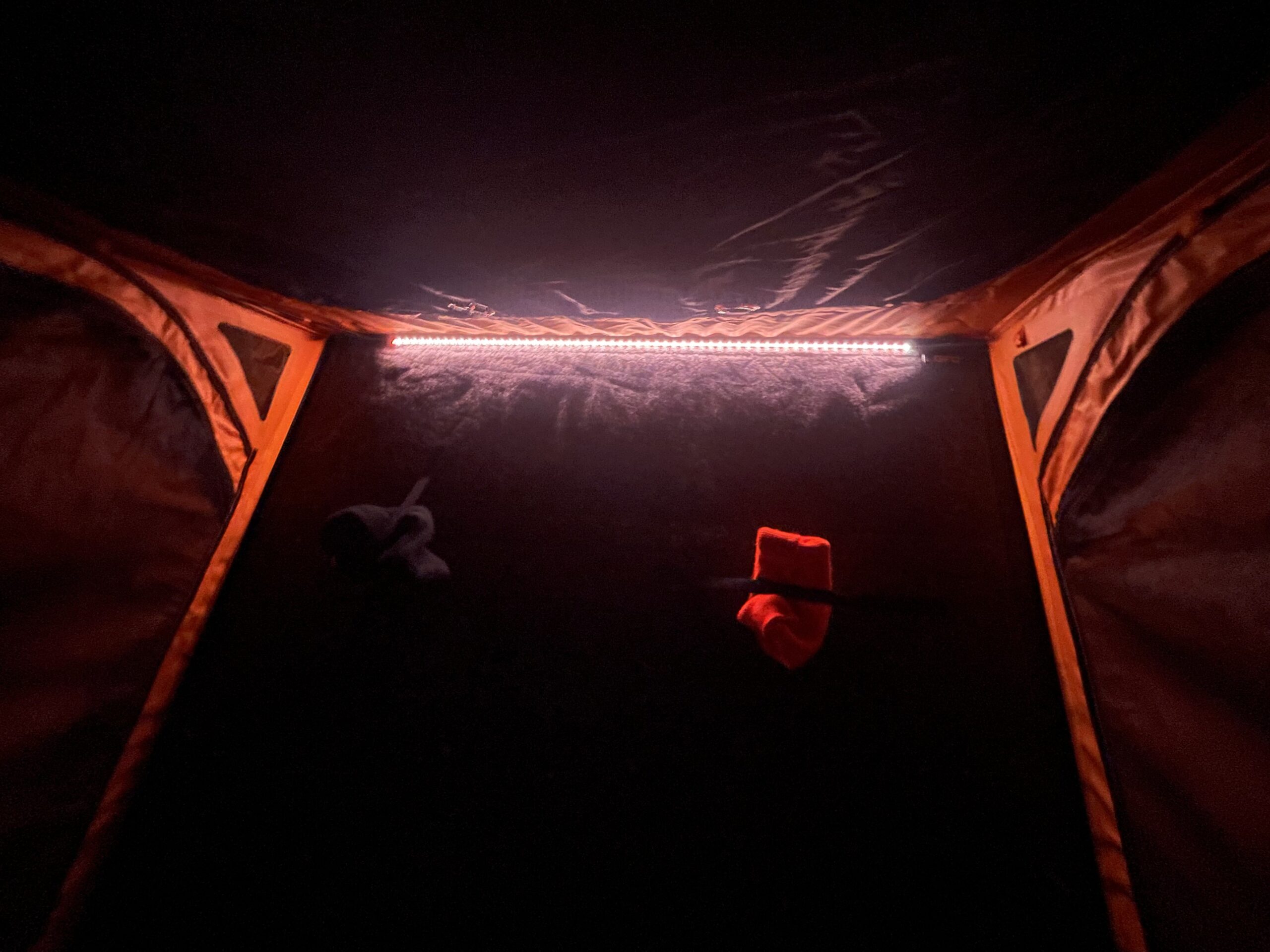 The dark inside of a tent with stocking hats, strapped by velcro to the roof, and an LED light rope on one corner