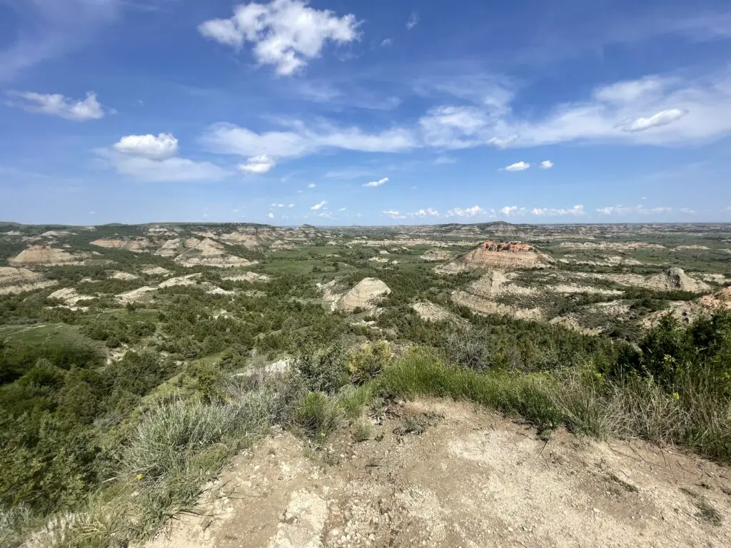 View from an overlook: green, grass-covered and tan, rocky mounds expand to the horizon, all under a blue sky