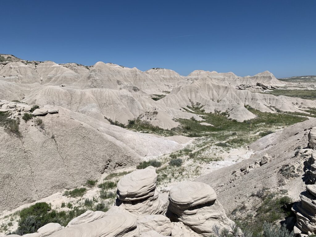Light-colored rock formations and rolling hills under a clear blue sky with sparse green vegetation scattered throughout the landscape.