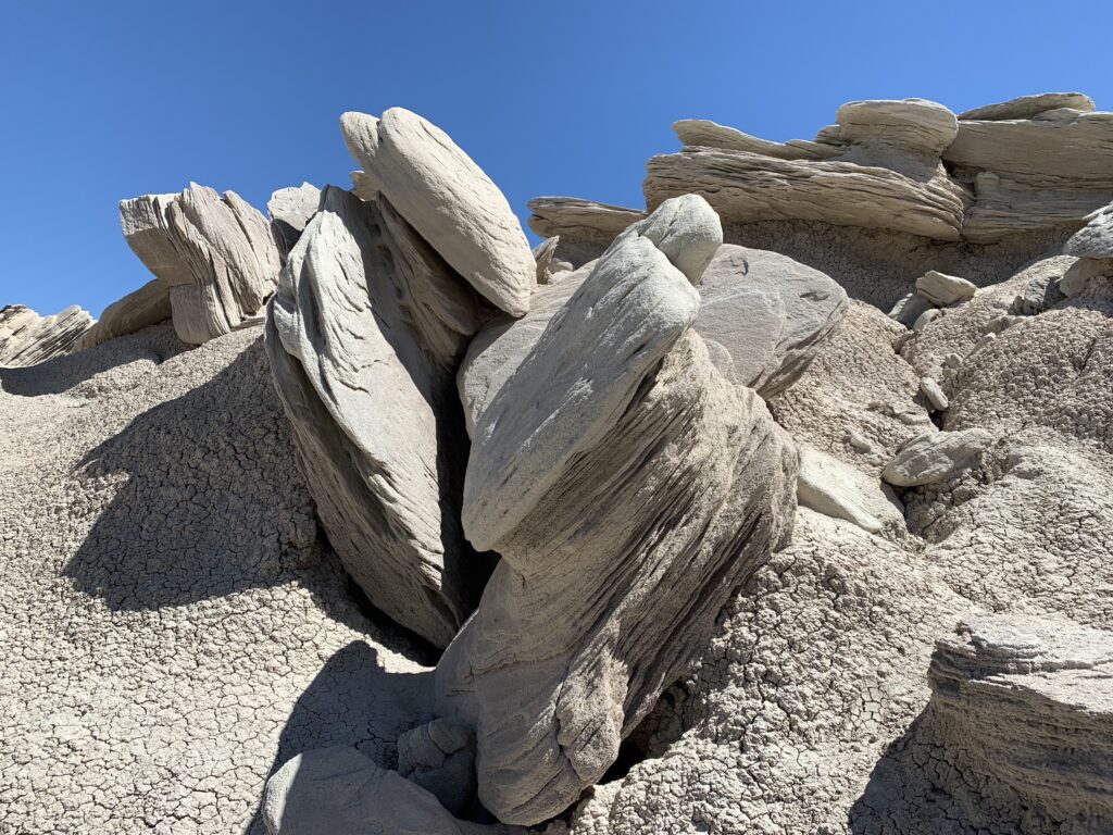 A short hill with large, flat rocks layered on each other that lay on their sides surrounded by light-colored gravel all under a clear, blue sky. 