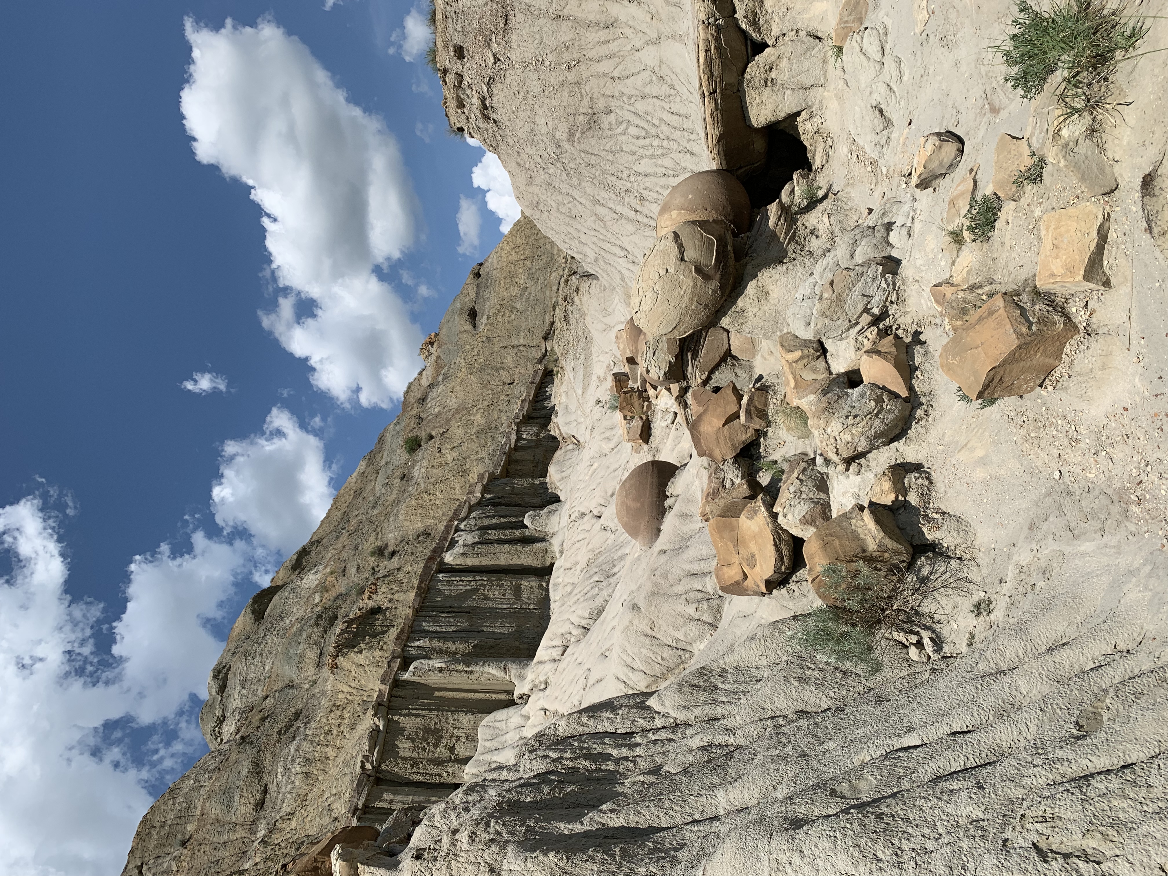 Rocky hill with large rocks that look like cannonballs water-falling down it, all under a blue sky with white, puffy clouds