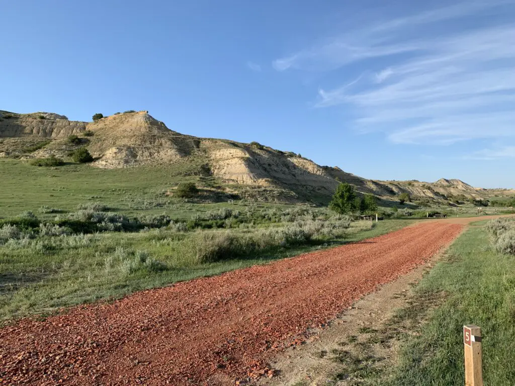 Red gravel drive surrounded by grass with a rocky hill behind, all under a blue sky