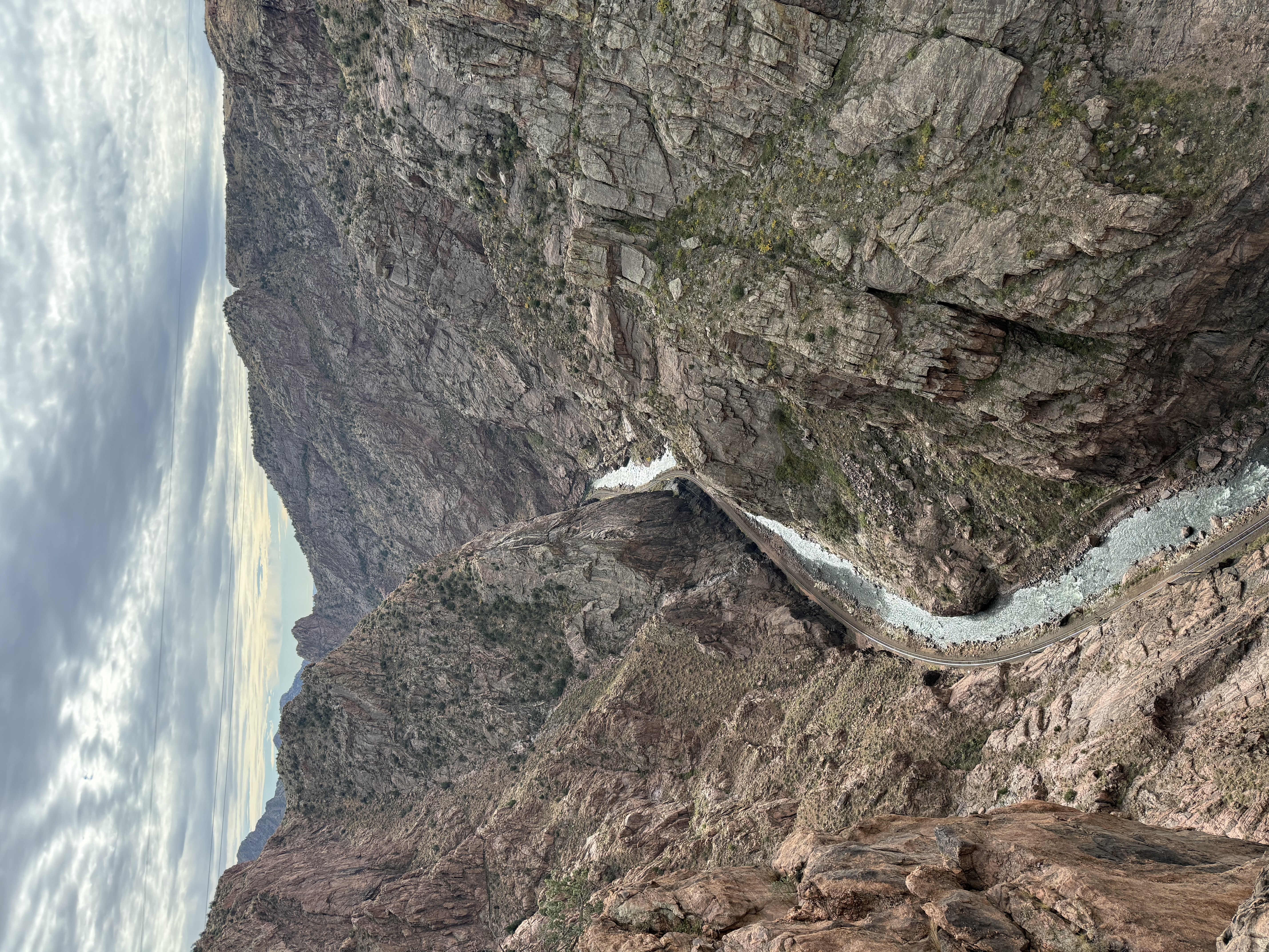 A winding river flows through a deep, rocky canyon with steep, rugged cliffs and sparse vegetation under a cloudy sky.