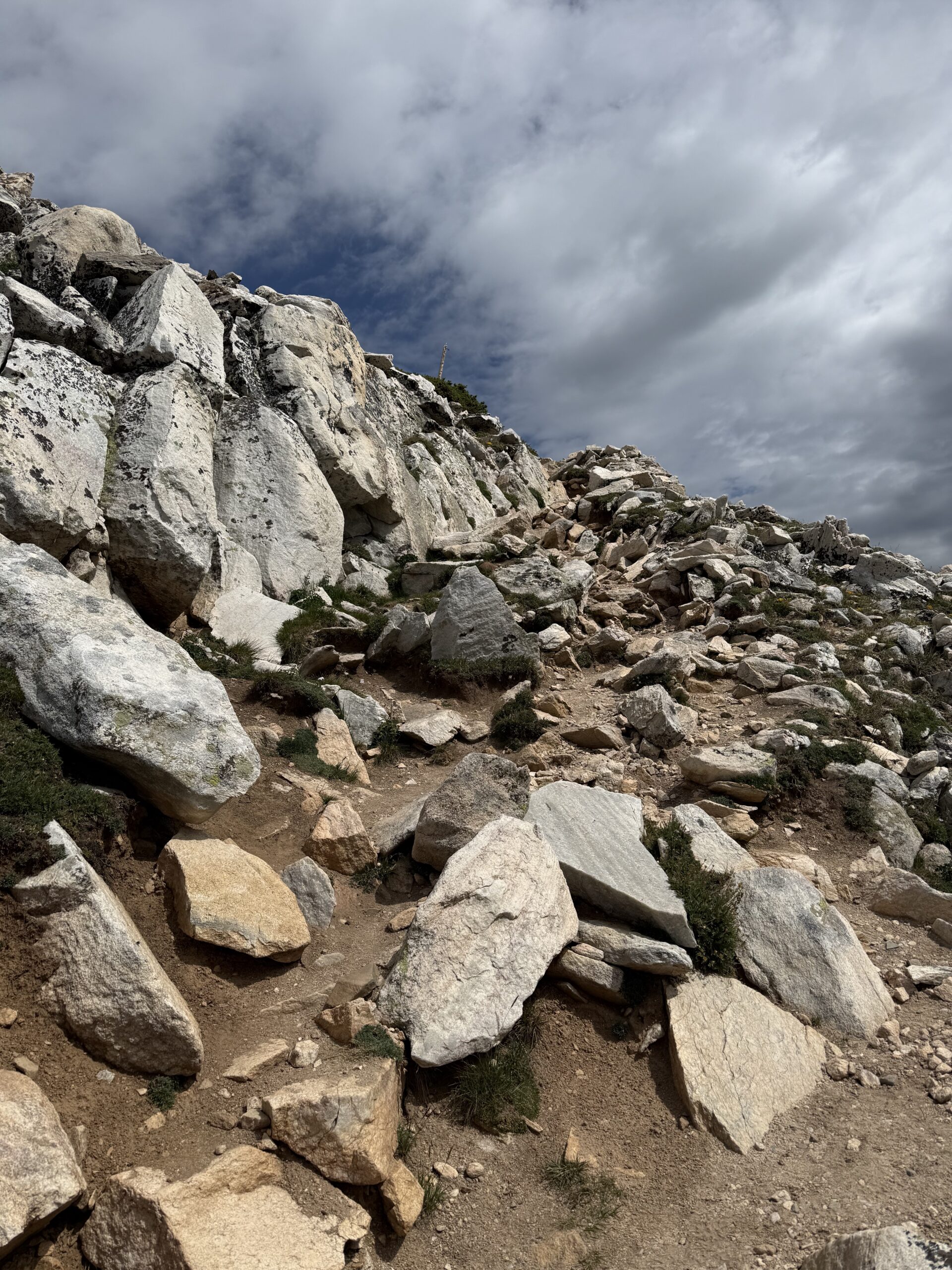 A very steep, mountain slope covered in large rocks with what appears to be a barely discernible foot path.